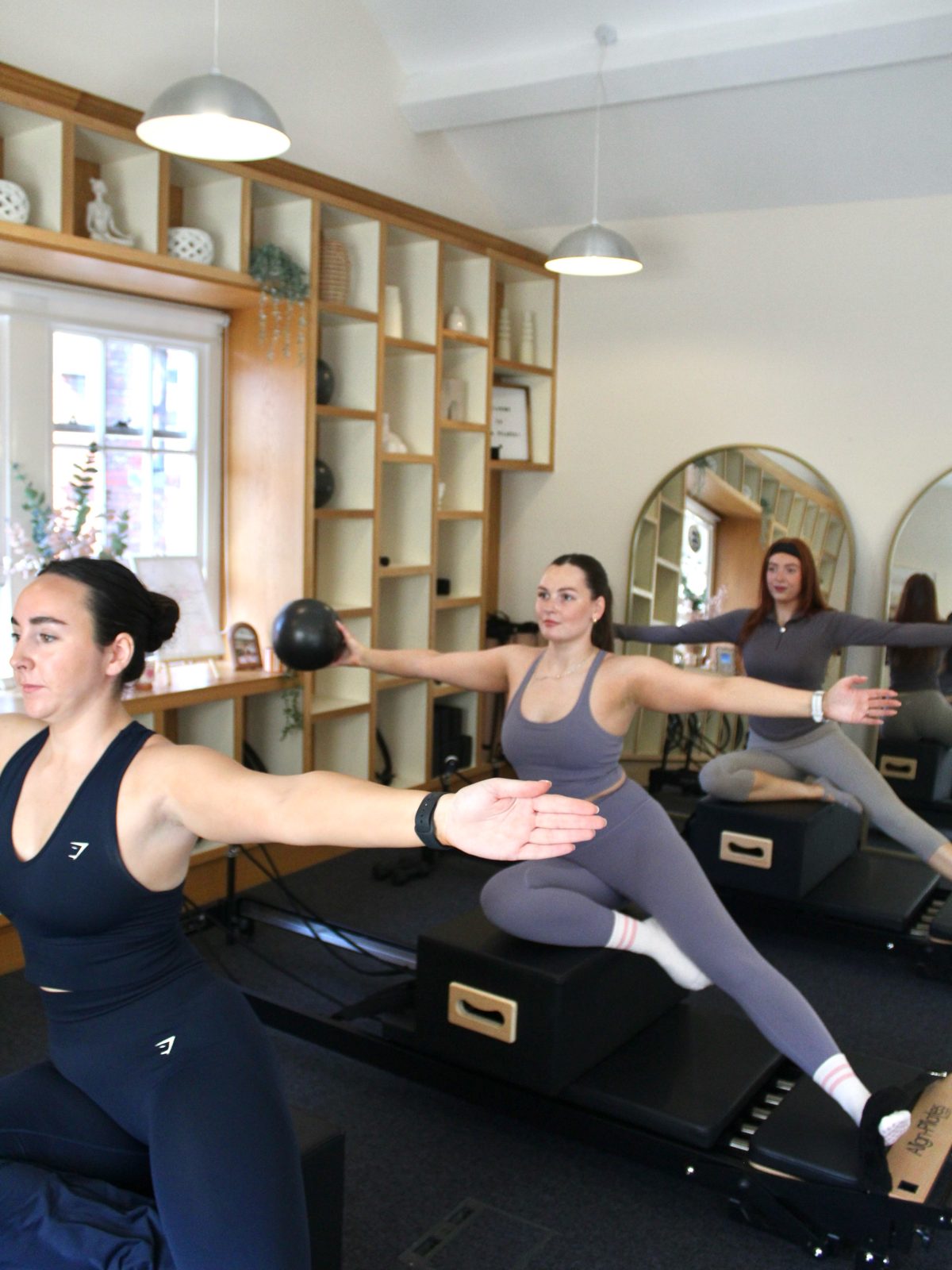 A small Reformer class in progress, three clients reaching out side by side