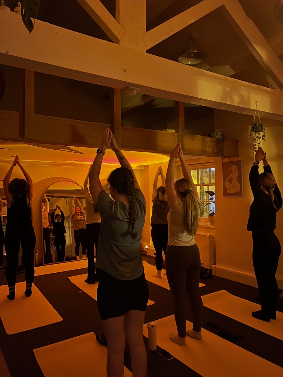 An evening yoga class at Casa Pilates, arms raised in warm low light
